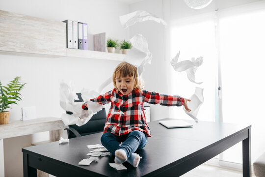 Mischievous girl playing with toilet paper on desk in home office