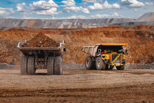 Two heavy dump trucks in open pit mine with gold ore carrying ore for industrial transport background and construction banner