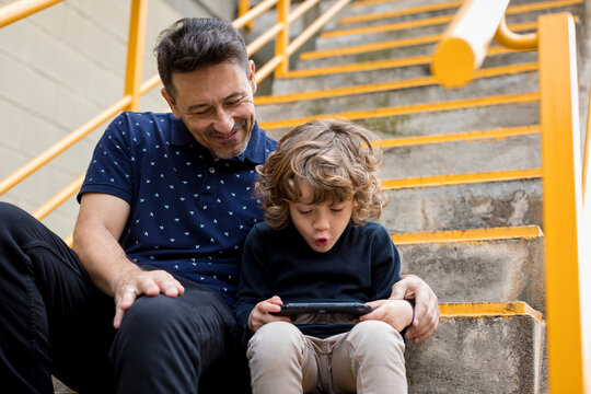 Father watching son playing with handheld game console
