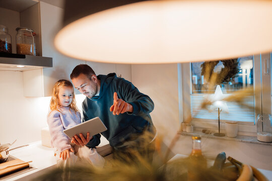 Father sharing tablet PC with daughter in kitchen