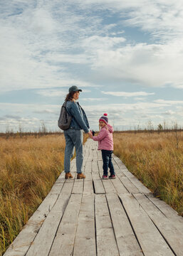 Joyful mother and daughter walk on autumn outdoor boardwalk