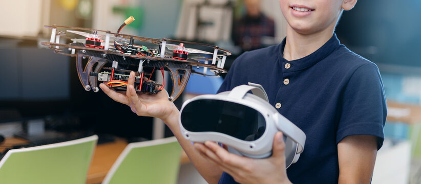 Teen boy holding drone and vr headset in workplace of innovation lab, STEM education future technology
