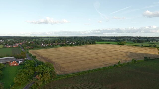 Rural farmland and harvested crop fields near countryside village. Drone flying above agricultural landscape with arable land and green fields at golden hour. Agronomy farming and sustainable