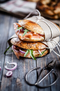 Two garnished home-baked bagels wrapped in paper and scissors on wood
