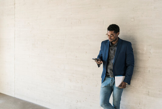 Businessman standing at concrete wall looking at cell phone