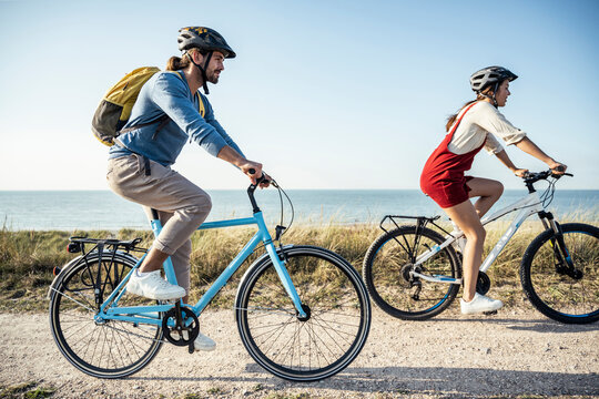 Couple wearing helmet riding bicycles against sea