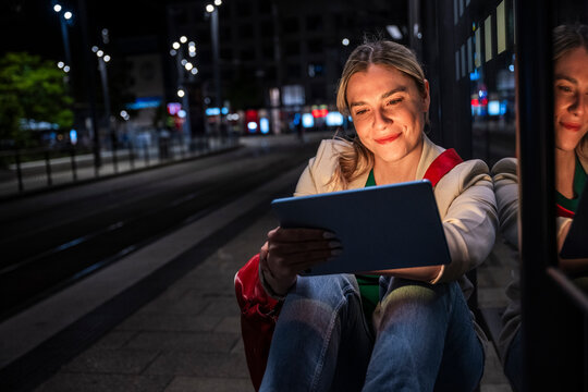 Smiling woman using tablet while waiting at tram station
