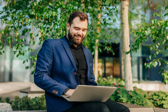 Smiling manager in suit working on laptop in park