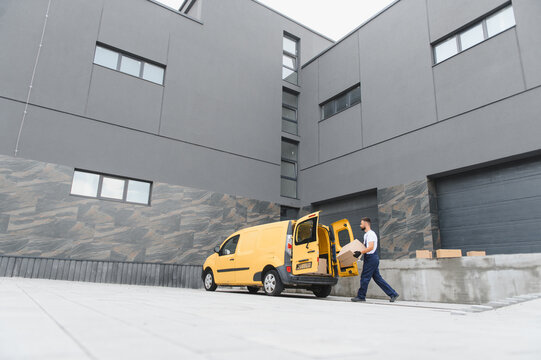 Delivery driver carrying cardboard box from yellow van