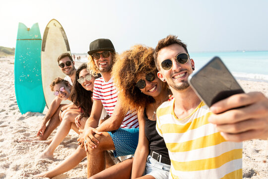 Friends sitting on the beach, having fun, taking selfies