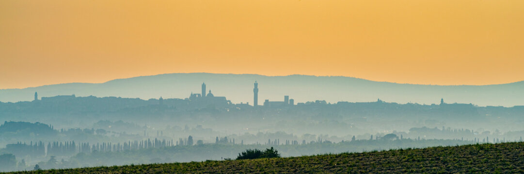 Italy, Tuscany, Siena, Panoramic view of hills and distant city at foggy dawn