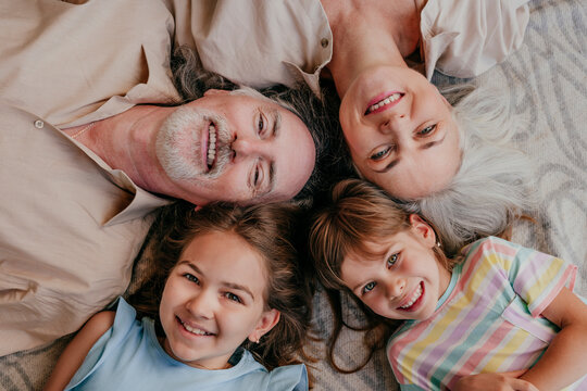 Happy grandparents and granddaughters lying together with heads in circle at home