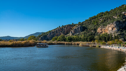 Fototapeta premium Excursion Boats Cruising the Dalyan River Below Ancient Lycian Rock Tombs
