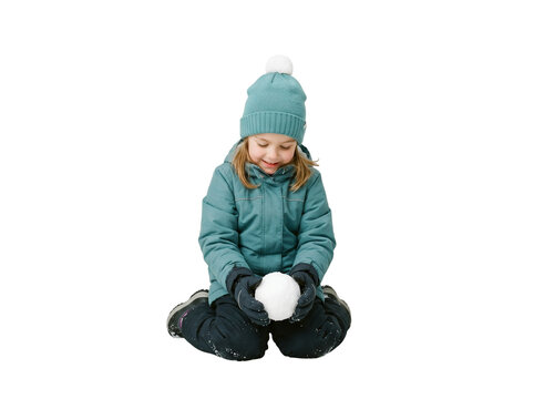 Isolated full body little girl sitting down in winter gear holding a fresh round snowball looking down and smiling