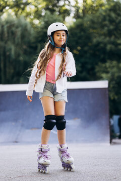 Young child wearing helmet and knee pads, confidently moving on rollerblades in a skate park during summer