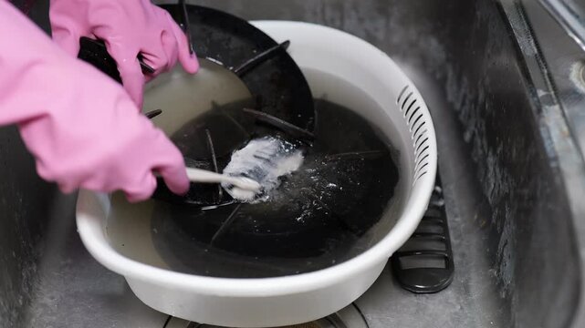 油で汚れたガスコンロの部品をキッチンシンクで洗う女性の手元