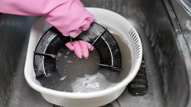 油で汚れたガスコンロの部品をキッチンシンクで洗う女性の手元