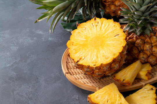 Fresh sliced pineapple fruits with green leaves over dark gray textured background.