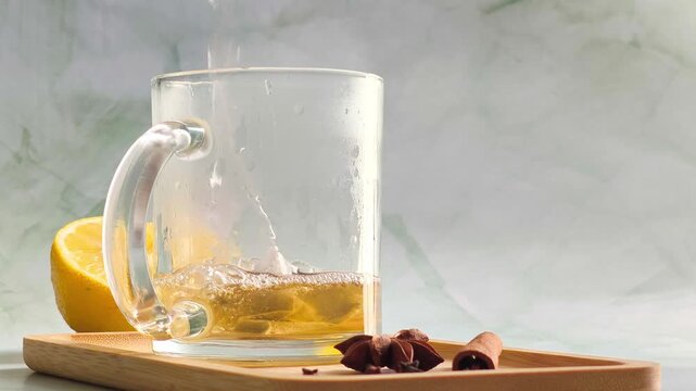 Hand pouring boiling water into clear glass cup over tea bag, dramatic steam and orange color infusion swirl close up