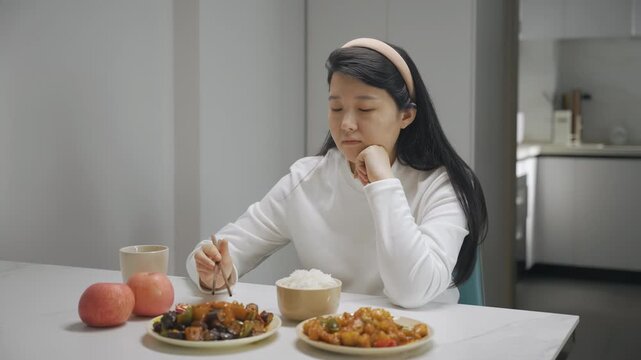 Portrait of unhappy lonely young woman sitting alone at kitchen table, looking despondent with disgust at plate of healthy food meal and vegetables, with no appetite, eating disorder, depression
