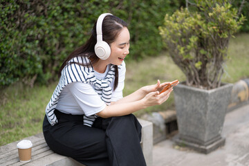 Obraz premium Smiling young woman using smartphone and headphones for online learning and remote work outdoors.