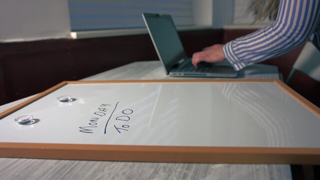 Monday morning schedule on whiteboard with woman typing on laptop background