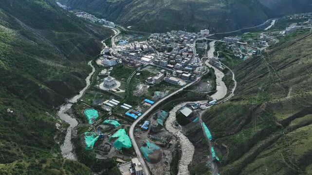 Aerial view of large intermountain town divided by winding river in steep valley of Daocheng Yading China