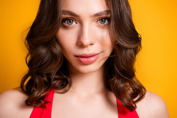 Fototapeta premium Young woman portrait with wavy brown hair and soft makeup wearing a red top against a vibrant yellow background, confident beauty close-up