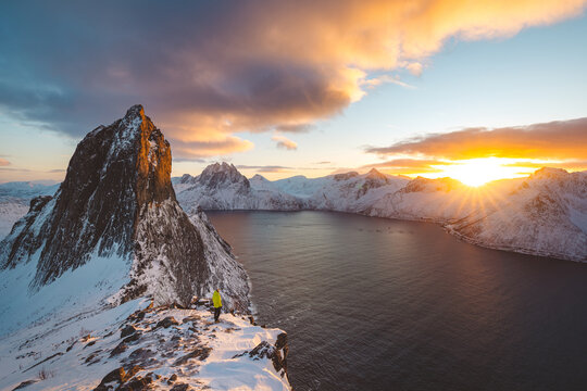 Hiker in a yellow jacket standing on a snowy ridge below Segla, Senja