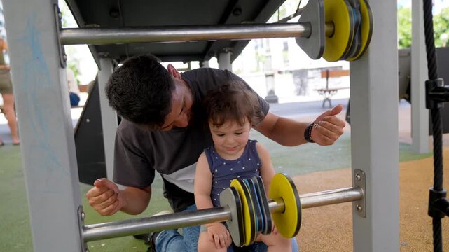 Caucasian father and his little toddler daughter laughing and playing together with an abacus at the playground, demonstrating a strong family bond and happy childhood moment in a city park