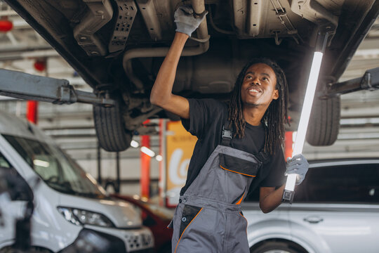 Mechanic checking the undercarriage of a car on a hydraulic lift, performing a thorough inspection of the vehicle