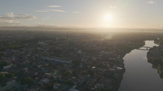 Drone footage orbiting left above Pasig River and Metro Manila during sunrise, revealing golden light, river reflections, and expansive urban scenery.