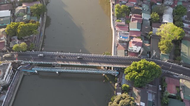 Drone footage moving left above a bridge crossing Pasig River, showcasing riverside neighborhoods and morning light in Metro Manila, Philippines.