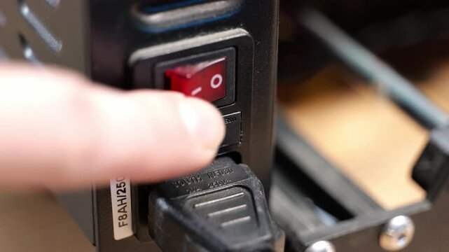 Static shot of a person pressing the power switch to the on and off positions on a device for safety testing.
