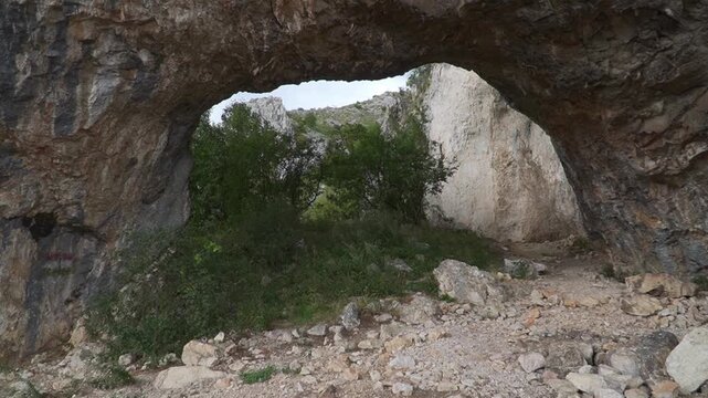 A rugged stone arch frames a view of greenery and distant cliffs, ideal for geology or nature projects.