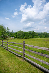 Obraz premium Split rail wooden fence aiong idyllic green pasture under blue sky treelined background ranch horse farm