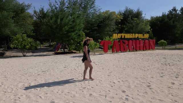 Indonesian girl walking on Tabuhan Island beach low tracking shot with surrounding sea view, East Java