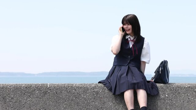 海辺でスマートフォンを使って通話する女子高校生