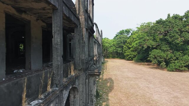 Drone advances close alongside multi-story bombed barracks facade on Corregidor island, blackened open floors, arched openings.