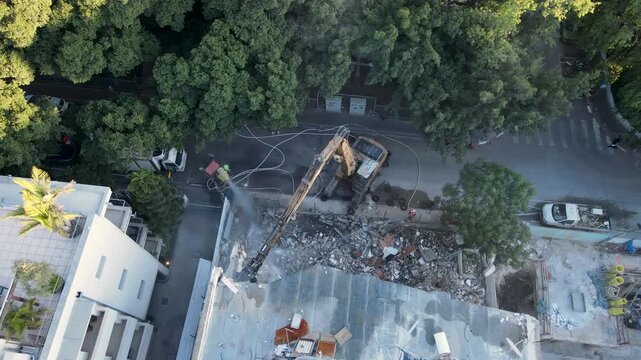 Top down aerial orbit of demolition operations and urban redevelopment work, drone descend as worker sprays water