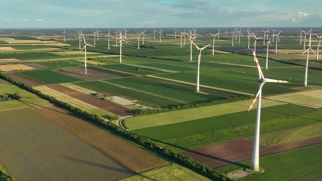 Slow rotating drone shot above a wind farm and agricultural landscape. Cinematic aerial footage showcasing renewable energy, sustainability and modern green infrastructure.