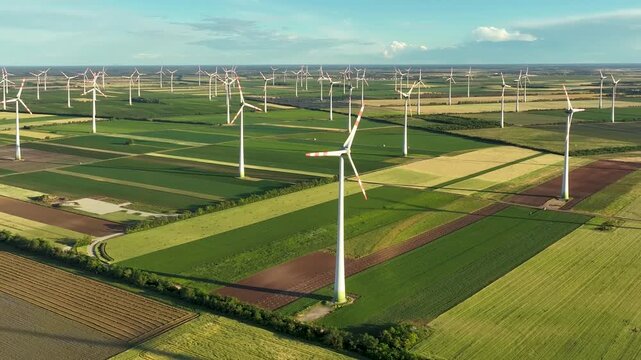 Static drone hover above a large wind farm and agricultural landscape. Stable aerial footage showcasing renewable energy, sustainability and modern green infrastructure.