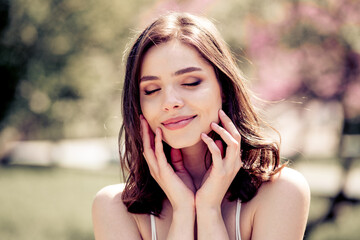 Fototapeta premium Young woman enjoying a peaceful outdoor portrait with eyes closed and gentle smile in a sunlit spring garden