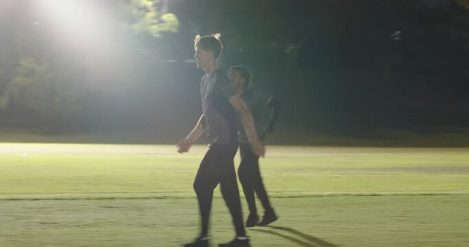 Teammates bouncing in floodlit huddle after fielder running to chase batsman swinging bat