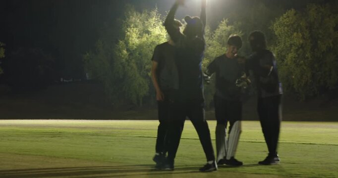 After winning run diverse cricket players walking celebrating under floodlights, pads gloves