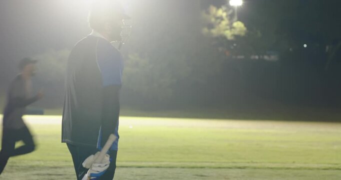 Male batsman reacting to ball, floodlights, walking off pitch, shaking bowler hand, copy space