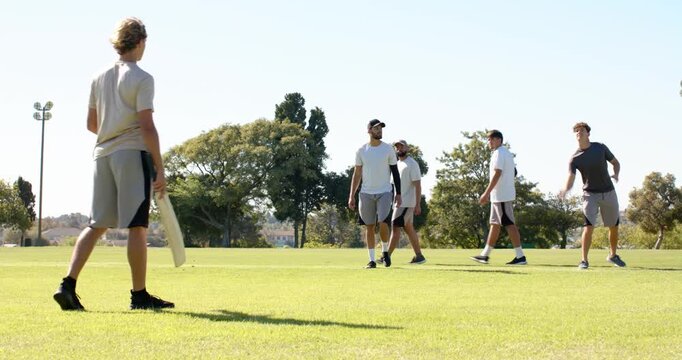 Diverse male friends playing frisbee on grassy park field, light pole in distance, copy space