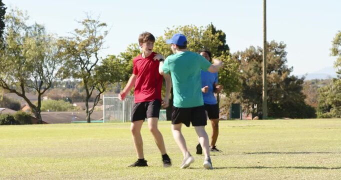Diverse male friends reacting to throw, diving, hugging, retrieving football, playing game