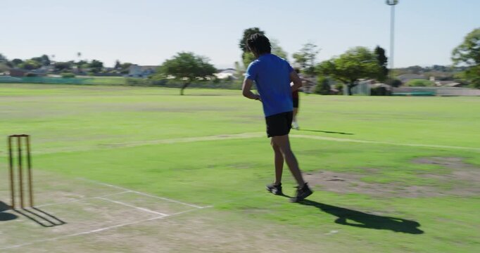 African american man pausing, running up, releasing ball for wicket on field, copy space