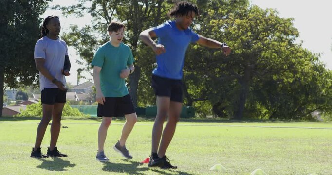 At stopwatch signal diverse male friends shuffling through disc cones on field testing agility